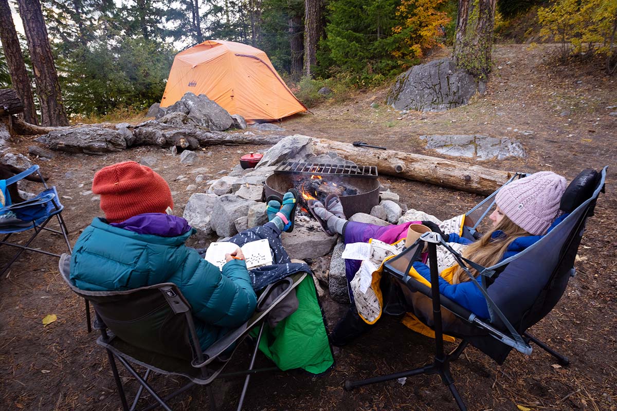 Two campers sitting in chairs by a warm campfire at night with camping blankets.