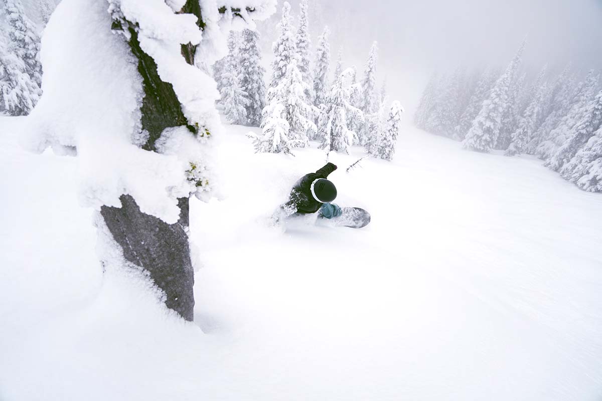 A snowboarder carving through deep powder with hands touching the snow.