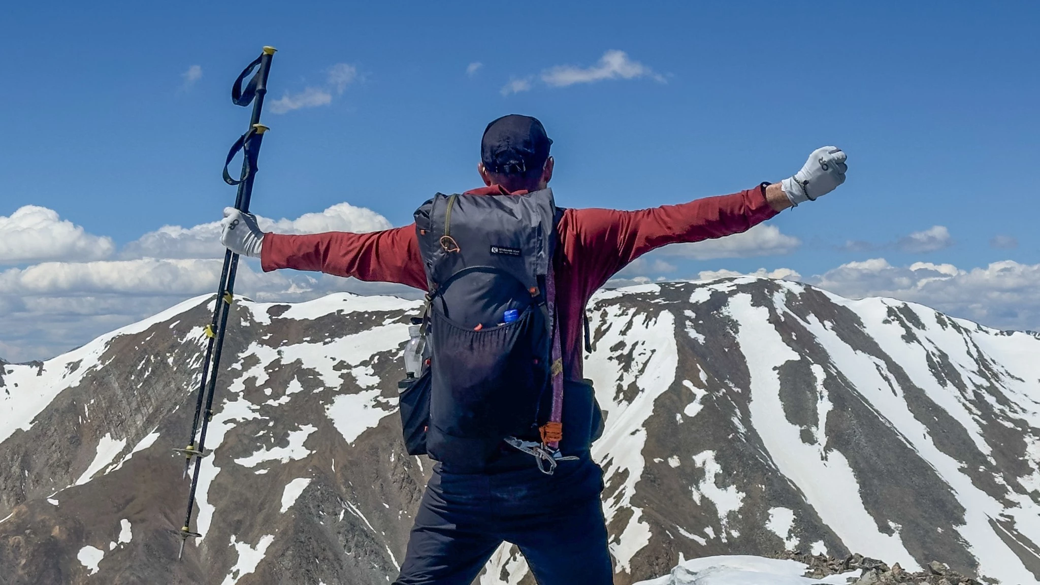 A thru-hiker wearing an ultralight pack ascends a steep mountain ridge under a clear sky.