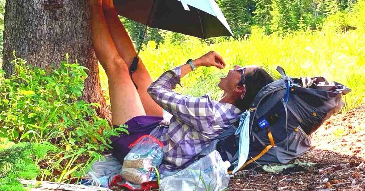 A hiker resting on the trail with their feet elevated, showing the soles of their hiking boots.