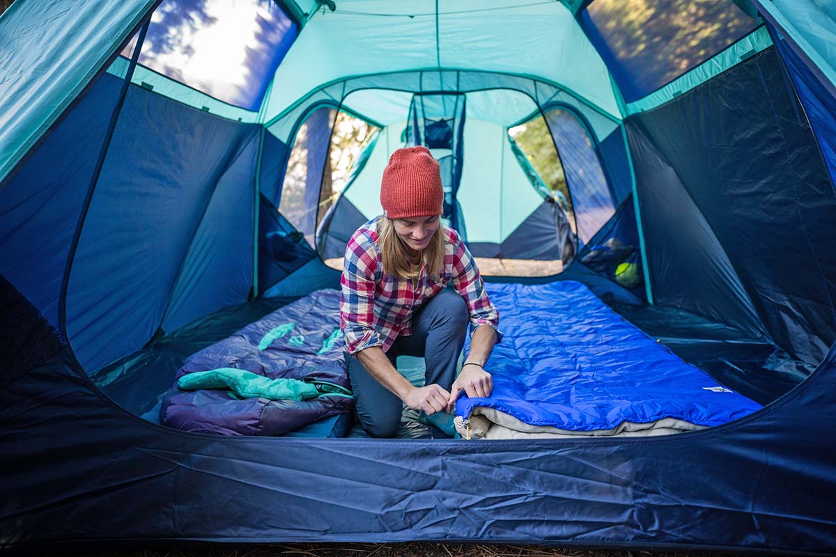 Two people setting up sleeping bags inside the spacious vestibule of a North Face Wawona 6 tent.