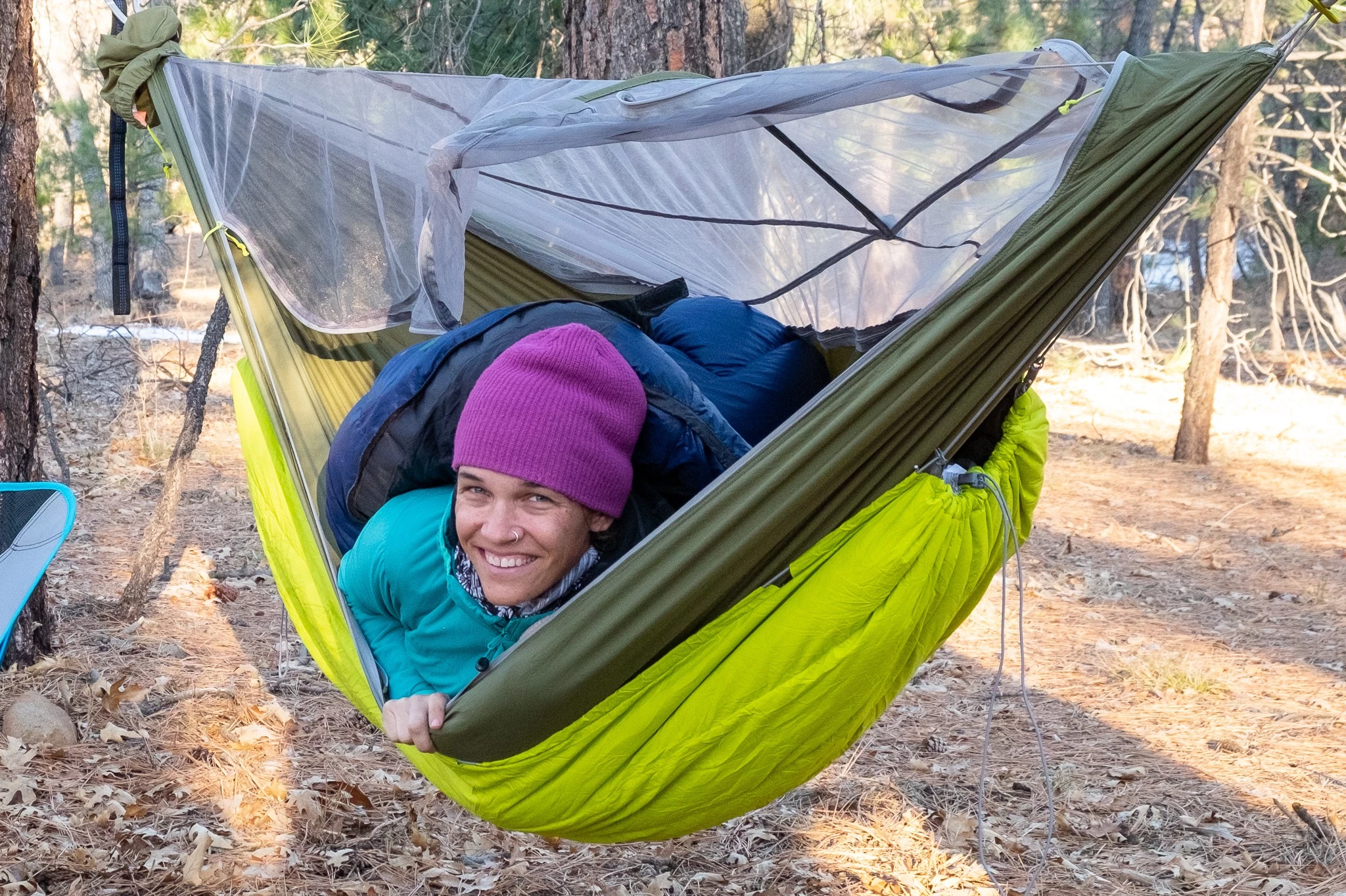 A camper cocooned in a blue hammock with an underquilt above a snowy ground.