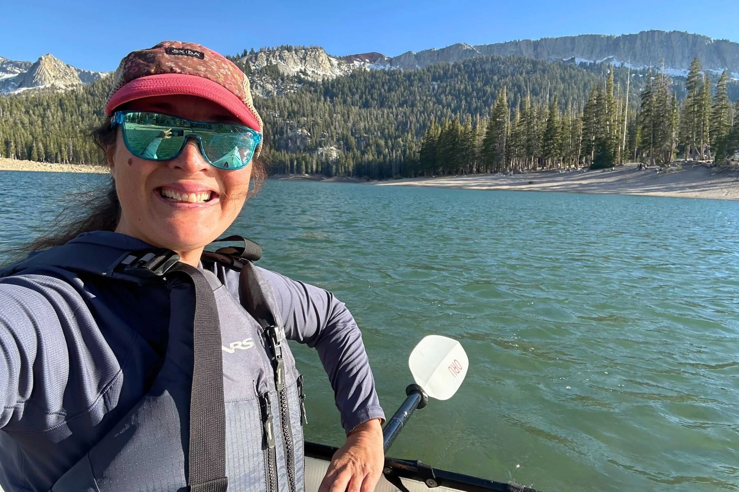 A person kayaking on a mountain lake wearing a grey REI Flash Shade sun hoodie.