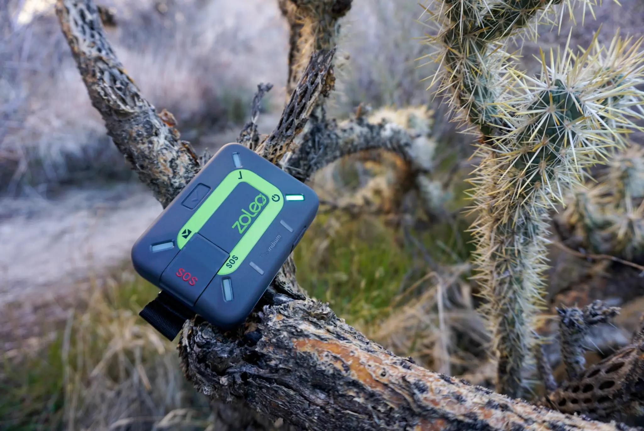A ZOLEO satellite communicator resting on a rock in a desert environment.