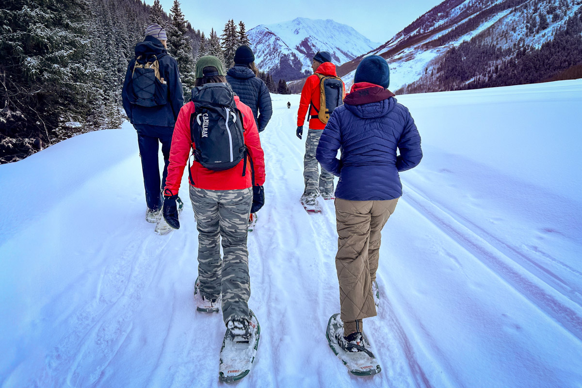 A group of hikers snowshoeing on a packed winter trail.