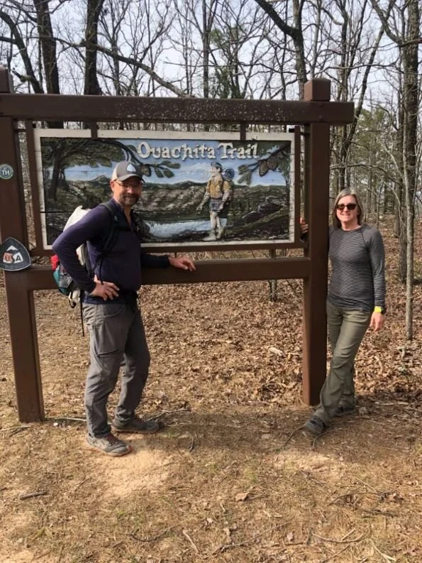 Two hikers standing and smiling next to the Pinnacle Mountain State Park trailhead sign at the eastern terminus.