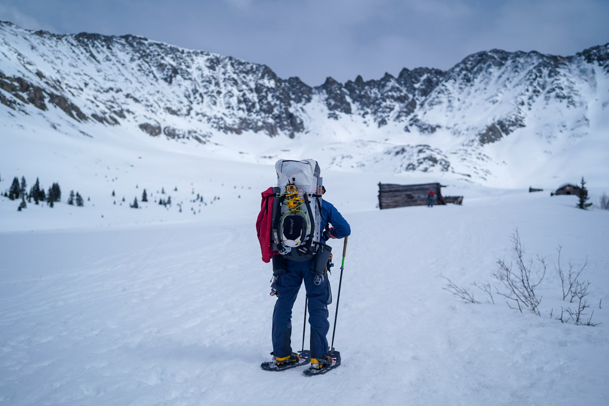 A man standing in a mountainous snowy landscape with snowshoes.