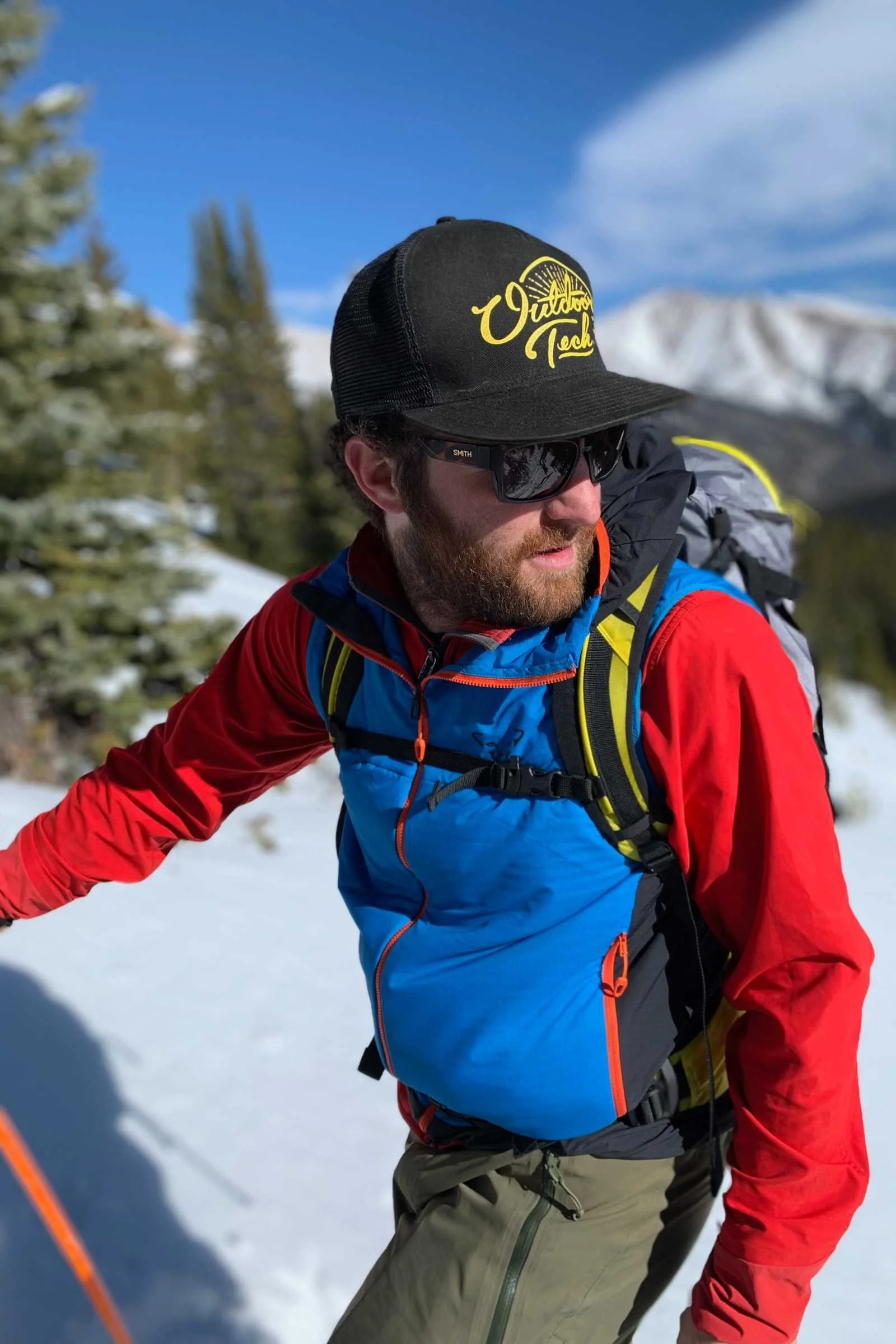 Male skier in technical gear standing on a mountain peak during a clear day.