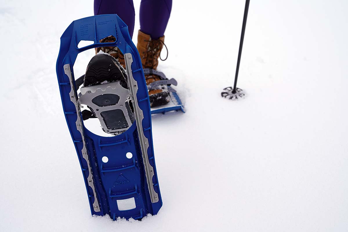 Close-up of the steel crampons and traction rails on the underside of a blue snowshoe.
