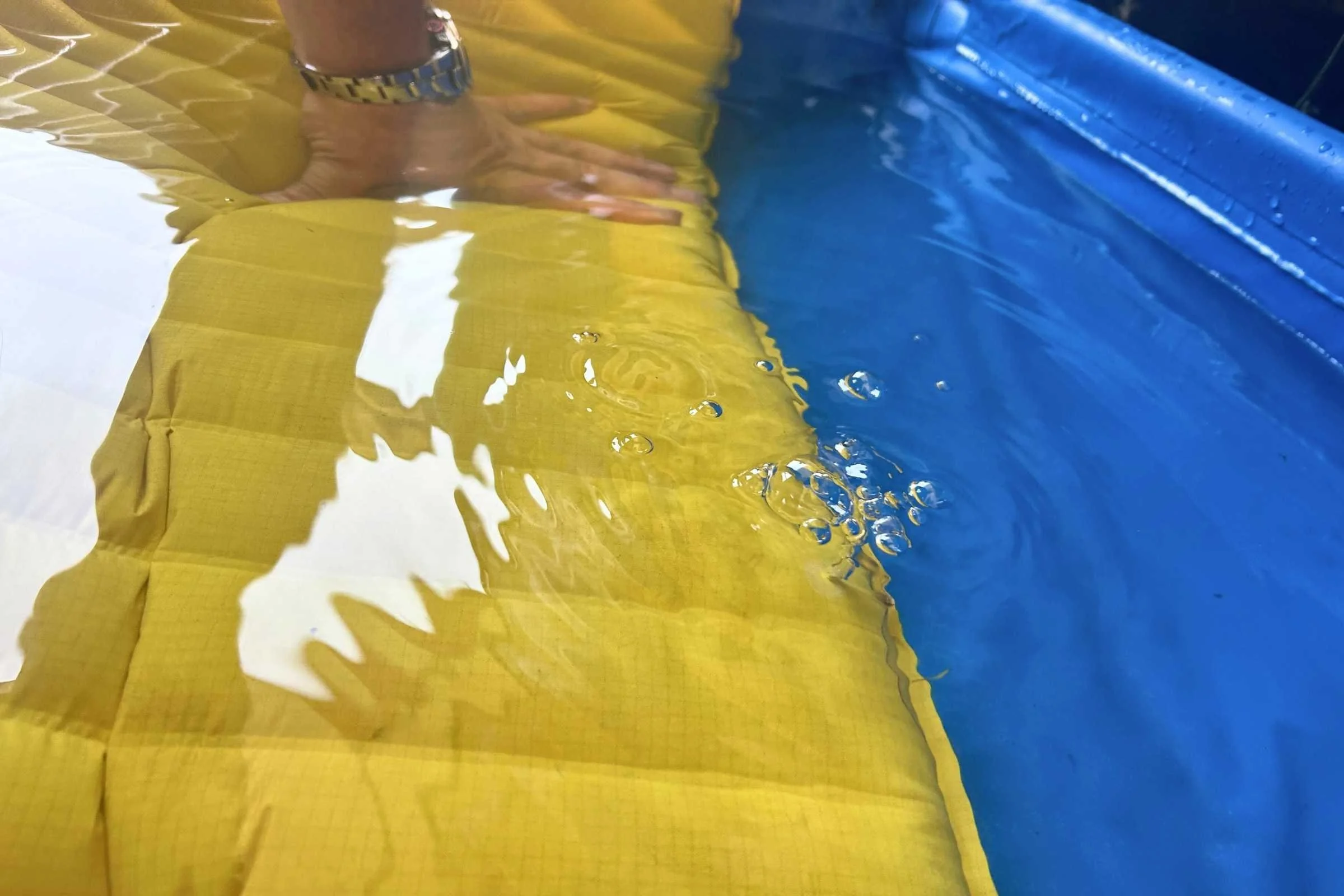 Air bubbles escaping from a submerged sleeping pad in a shallow pool.