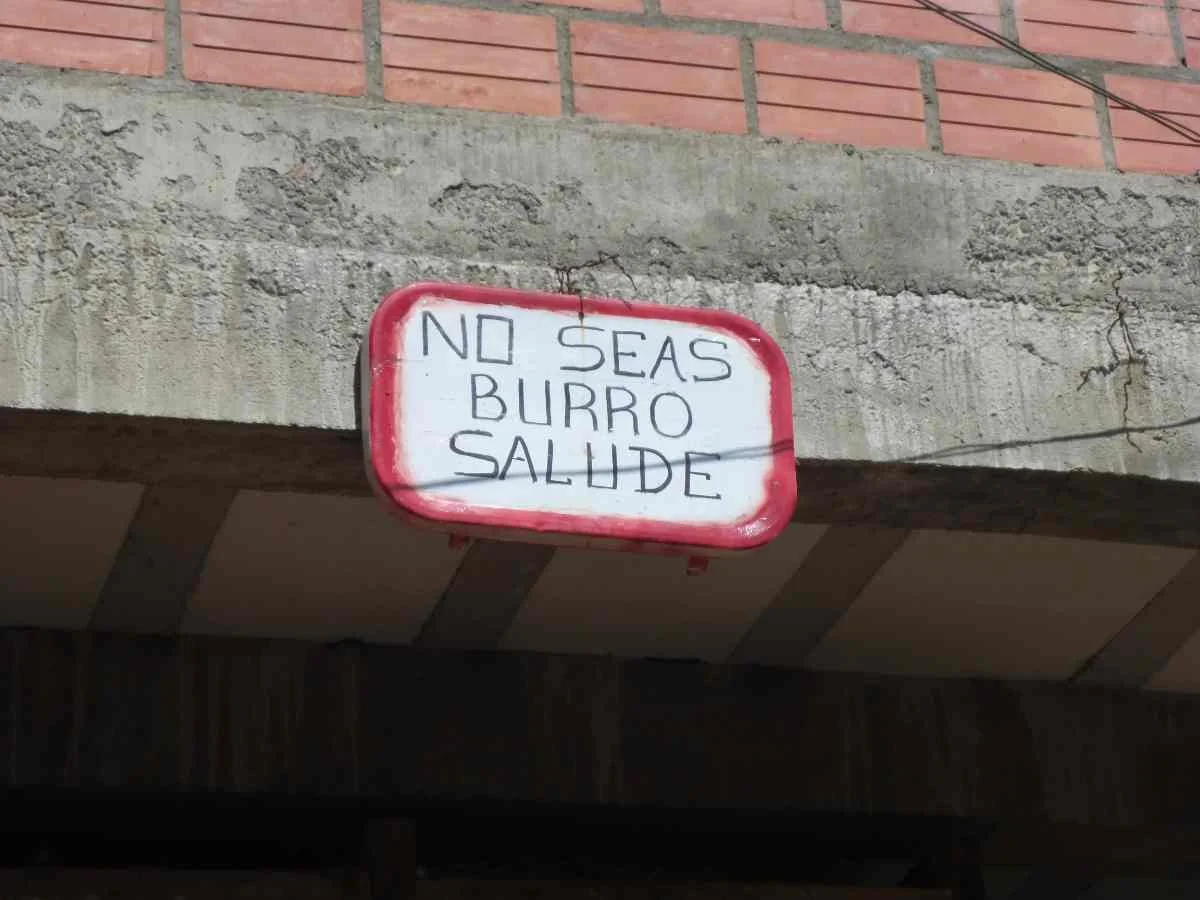 A colorful sign above a Bolivian market that translates to 'Don’t be a donkey, greet people.'