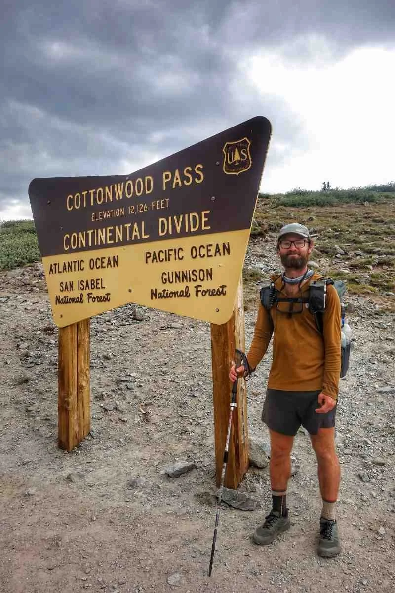 A hiker outfitted in a sun hoodie, hiking shorts, and trail running shoes standing on a trail.