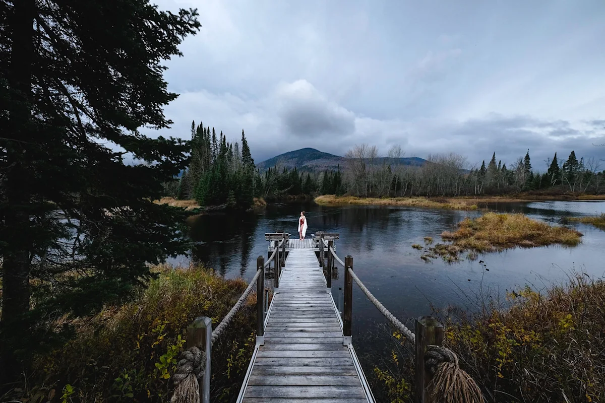 A wooden footbridge crossing a stream leading toward the Farouche forest cabins.