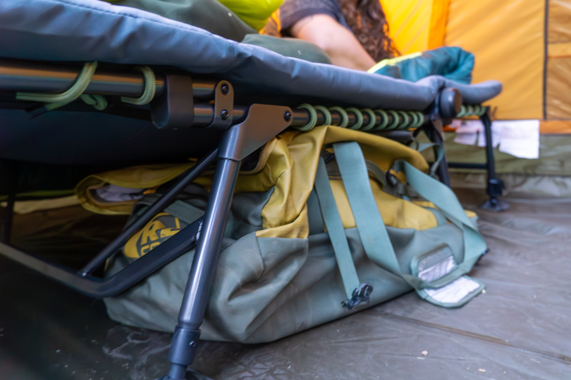 The REI Wonderland Comfort Cot inside a camping tent with a gear bag stored beneath the frame.