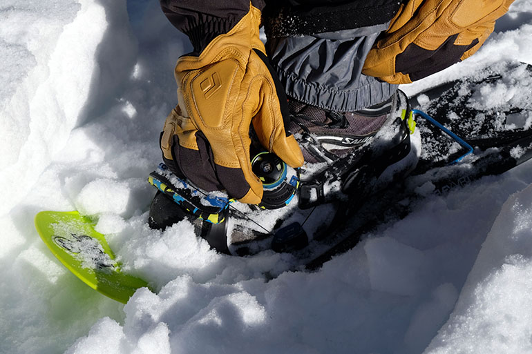 A close-up of a hand adjusting a Boa dial on a snowshoe binding.