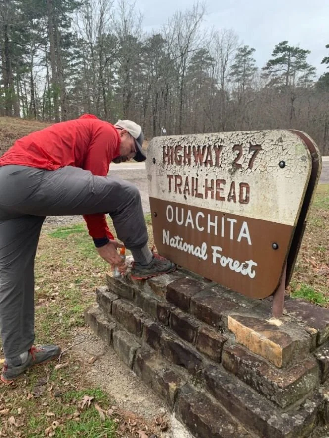 A hiker applying insect repellent to their socks and hiking shoes.