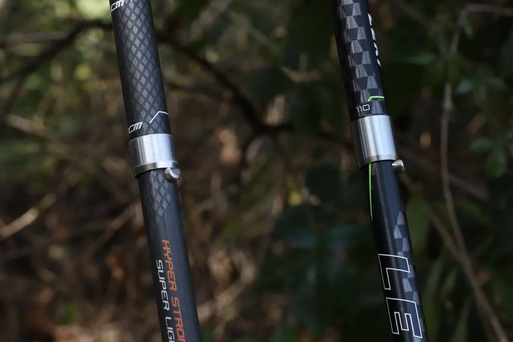 Comparative view of two trekking poles, one carbon fiber and one aluminum, side by side.
