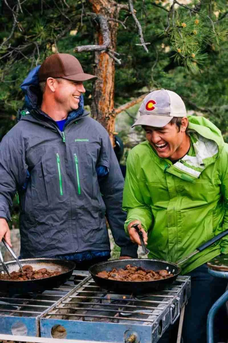 A set of stainless steel camping pots and pans nested together in a compact stack.