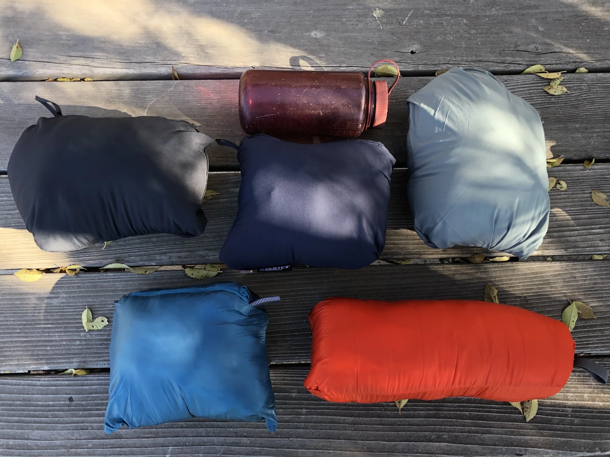 Five different insulated jackets compressed into their own pockets next to a Nalgene bottle for scale.