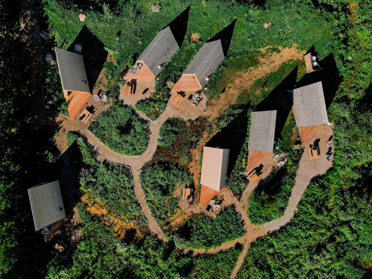 Aerial view of a row of micro-cabins nestled between a river and the forest at Farouche.
