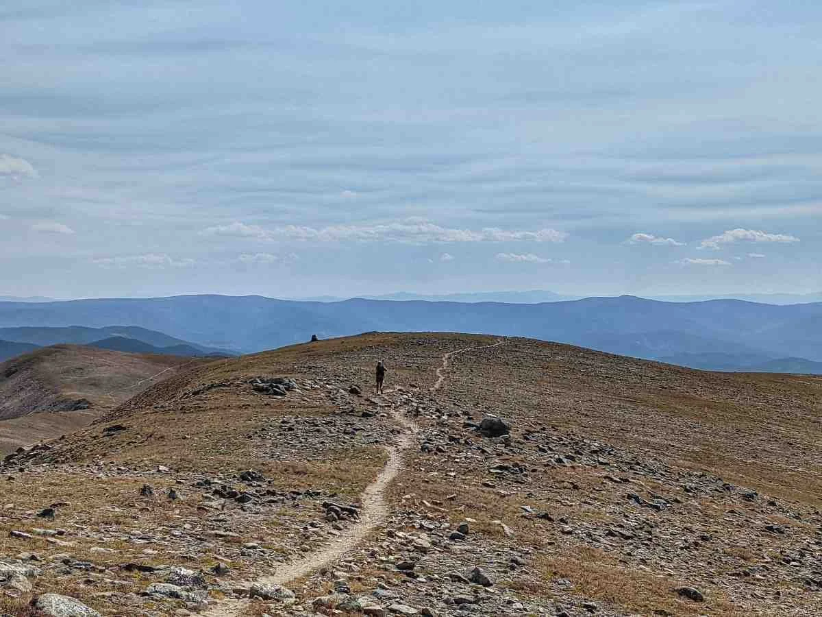 Long, winding trail through rocky terrain above the tree line with distant mountains.