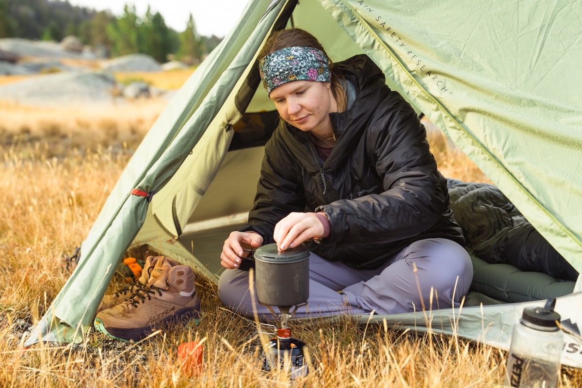 A woman making coffee in a tent wearing a thick Patagonia DAS Parka.