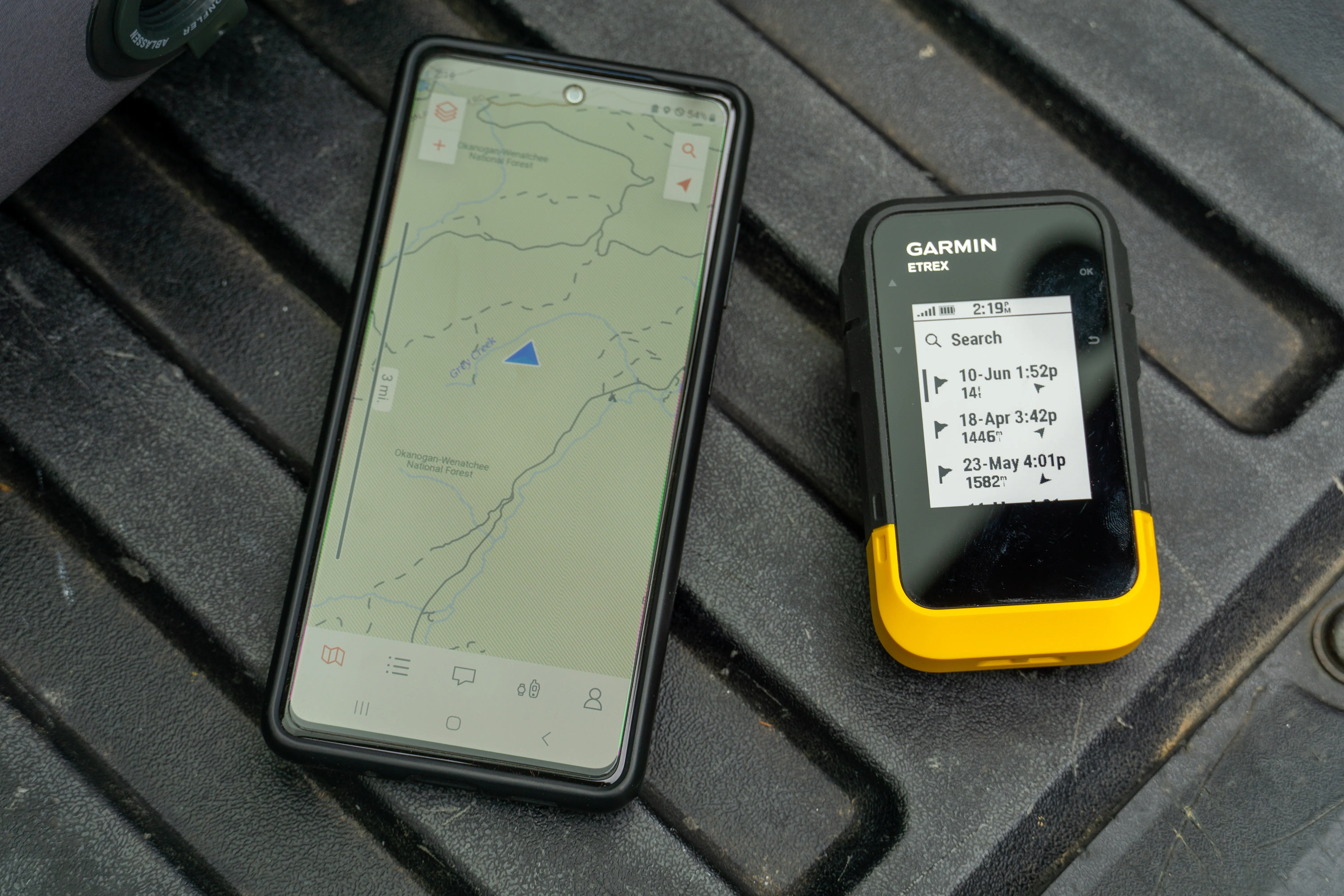 A smartphone and a Garmin GPS unit placed side-by-side on a trail map to show app syncing.