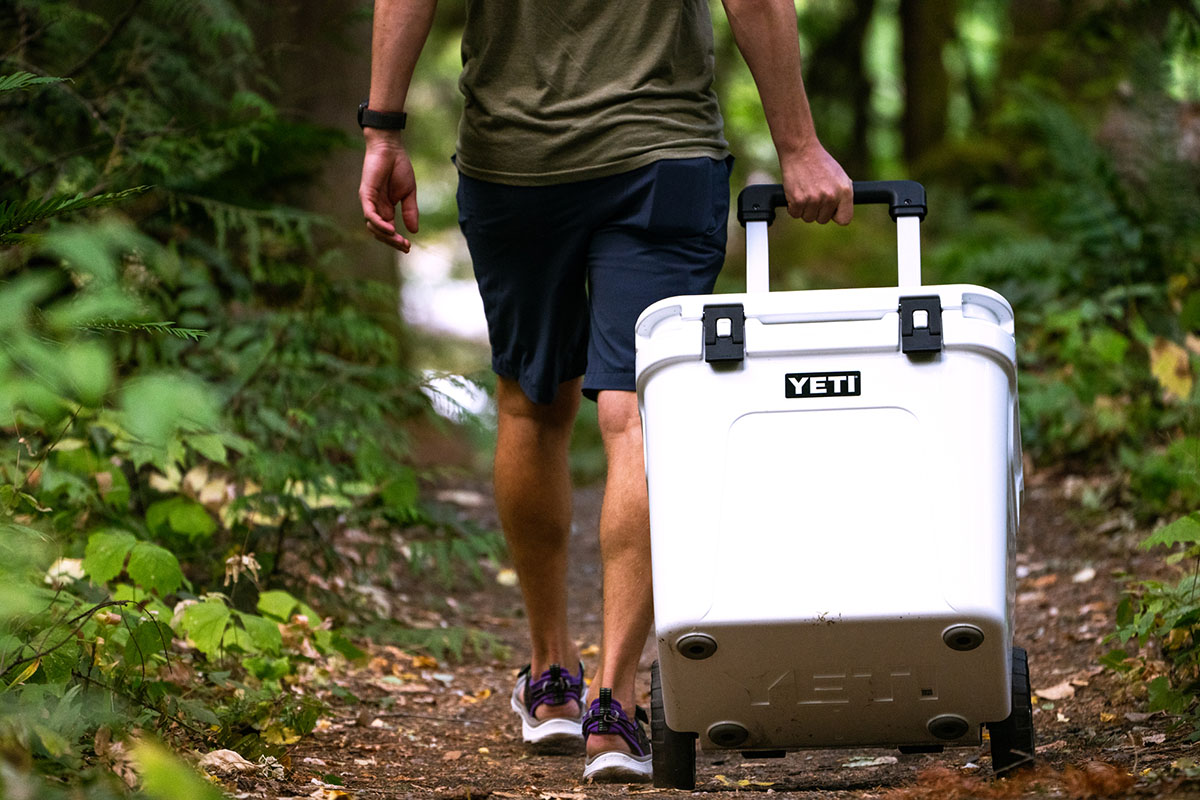 A camper pulling a Yeti Roadie 48 wheeled cooler across a grassy campsite.