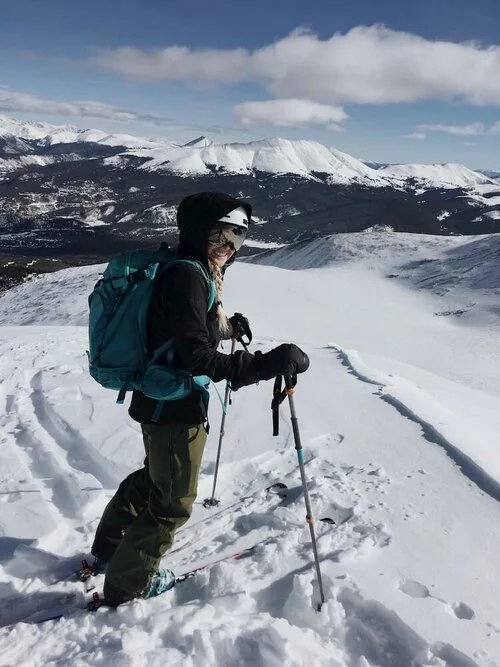 A skier descending a wide open alpine slope on a clear day in Colorado.