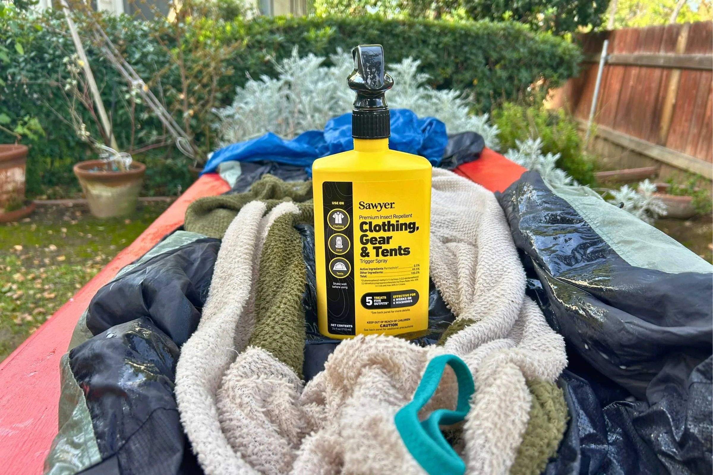 A hiker applying Permethrin treatment to their technical hiking shirt and gear outdoors.