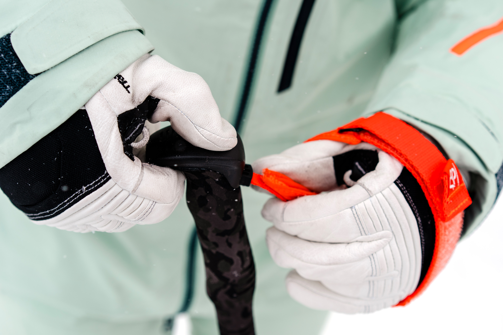 A person wearing ski gloves while precisely adjusting a pole strap.