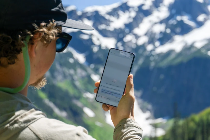 A person using a smartphone connected to a satellite network in a snowy forest.