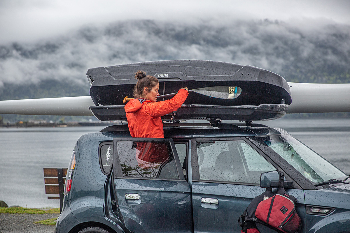Two people unloading outdoor gear from a Thule rooftop cargo box mounted on an SUV.