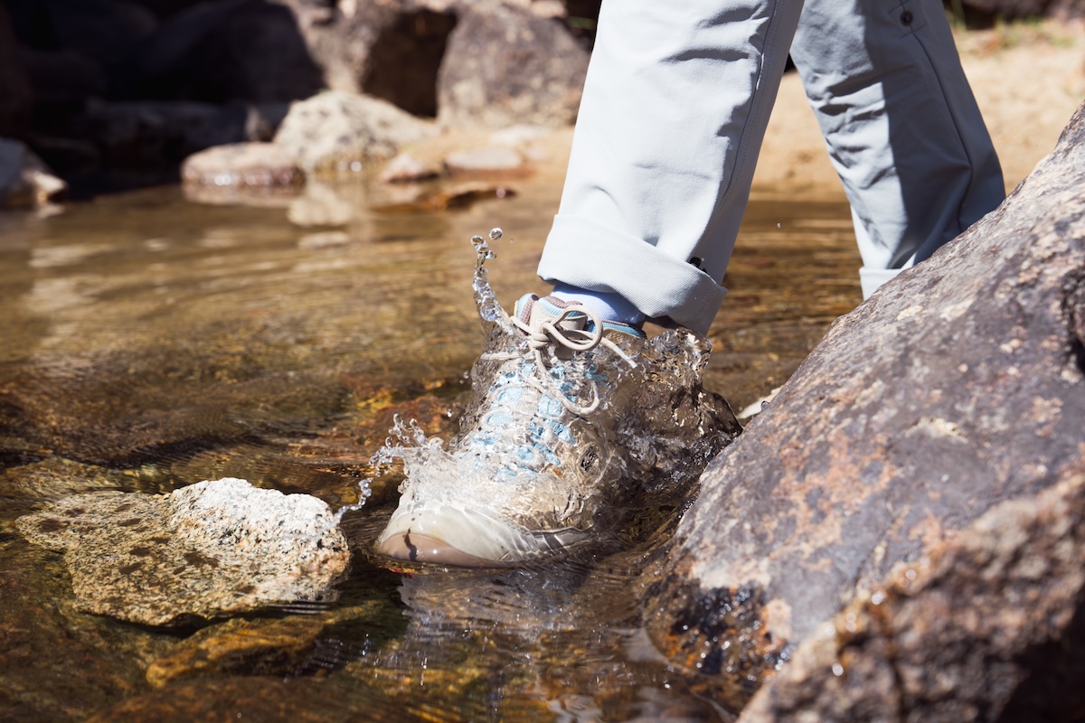 A close-up of waterproof trail shoes submerged in a shallow river.