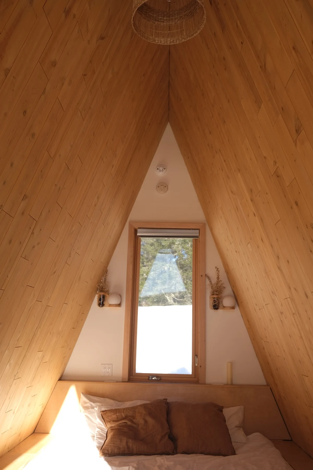 Inside a Farouche micro-cabin showing a large bed and light wood minimalist interior.