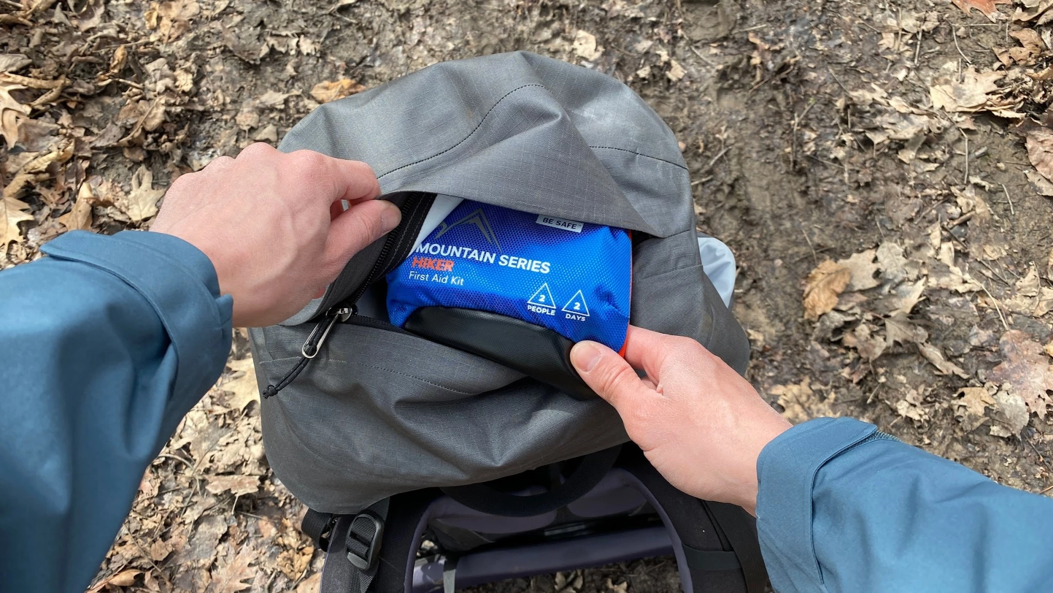 A lightweight compact first aid kit held by a hiker in a mountain wilderness setting.