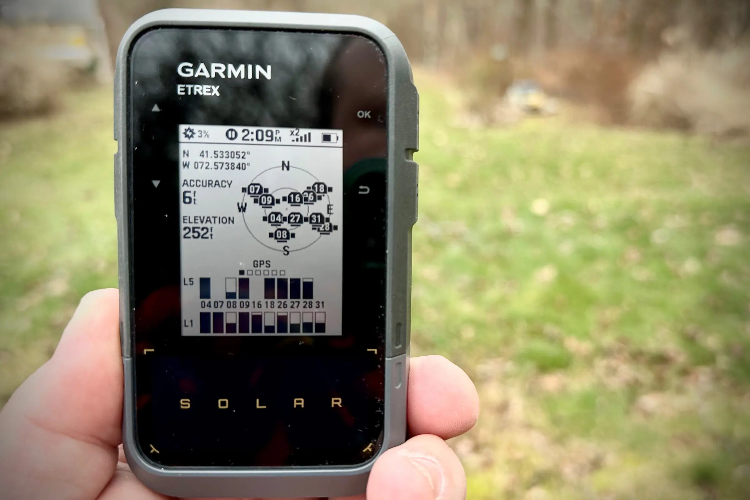 Hands holding a GPS device showing the satellite signal strength and acquisition screen.