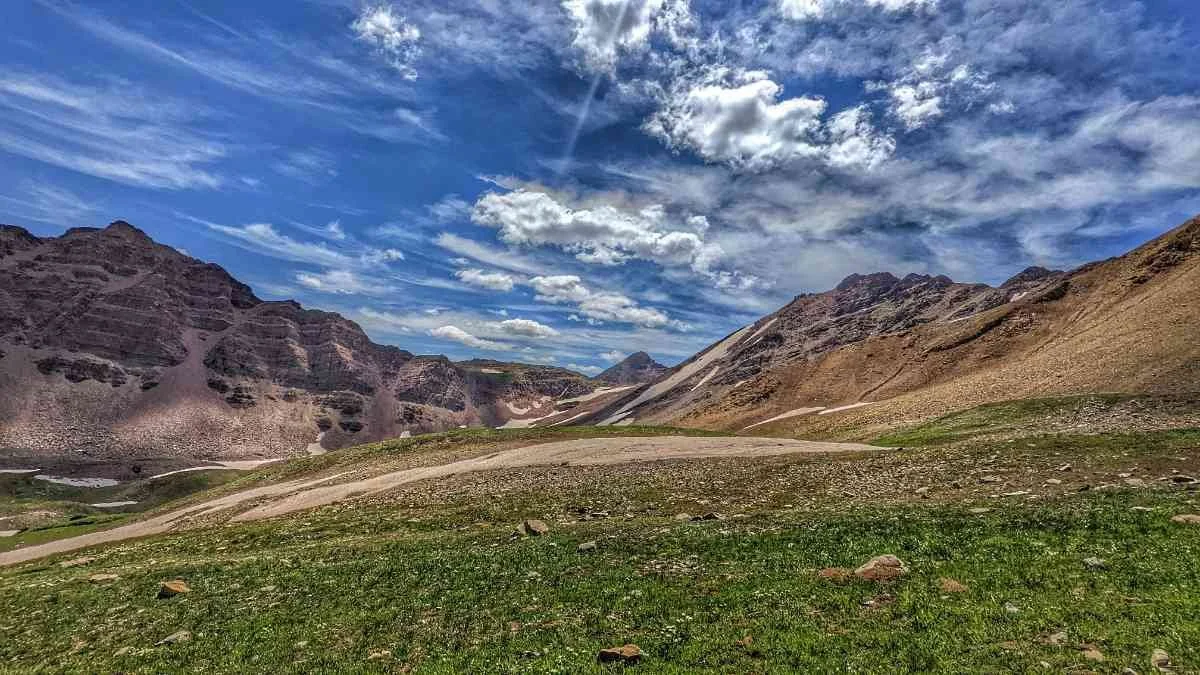 Tents pitched in a designated camping area near the turquoise waters of Snowmass Lake under a clear afternoon sky.