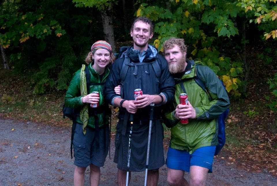 Three hikers smiling in wet conditions while wearing various technical layers.