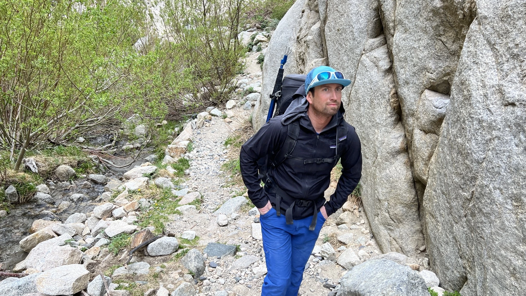 A man wearing a trim-fitting blue softshell jacket while hiking upward.