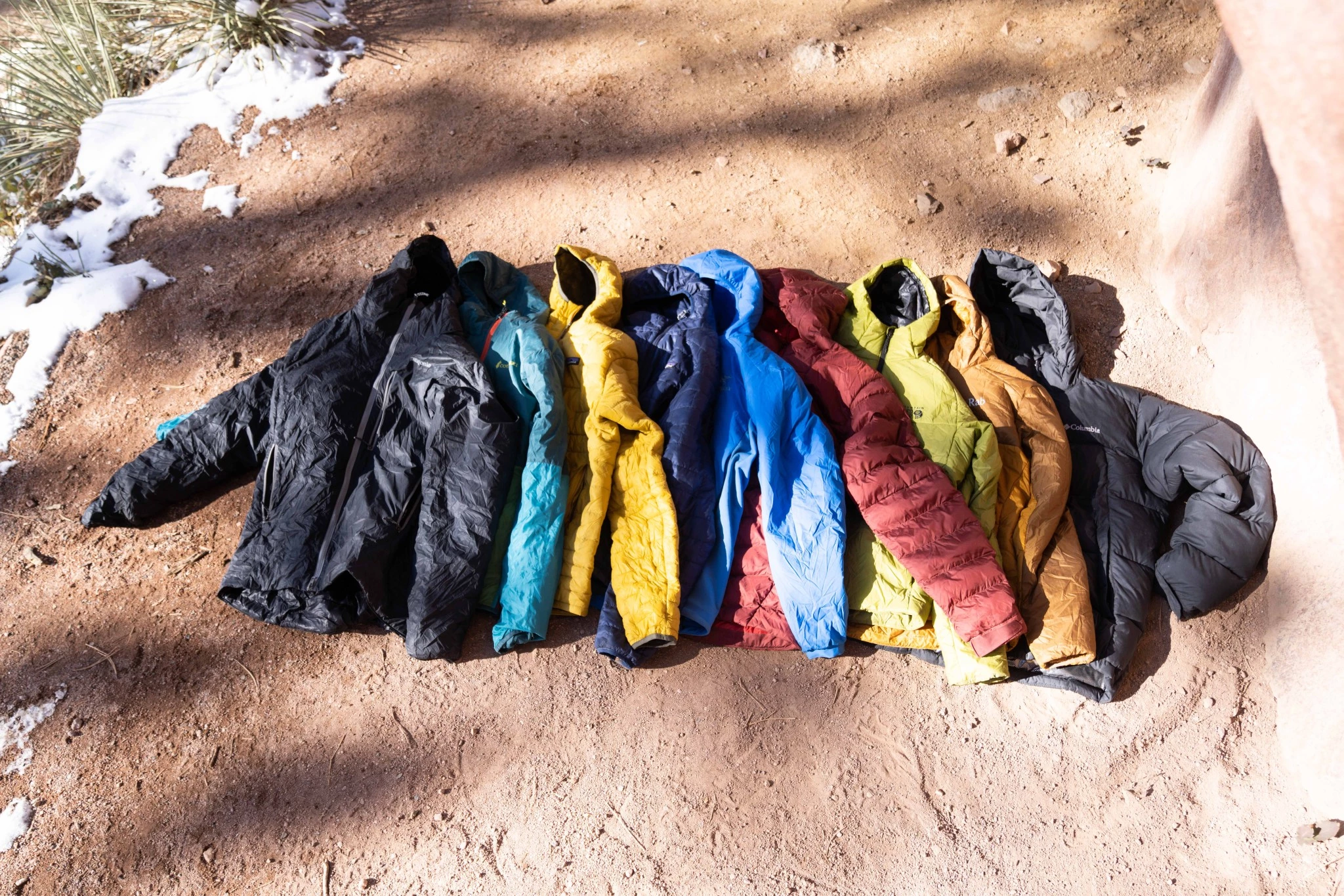 A selection of several high-end men's insulated jackets being compared in an outdoor setting.