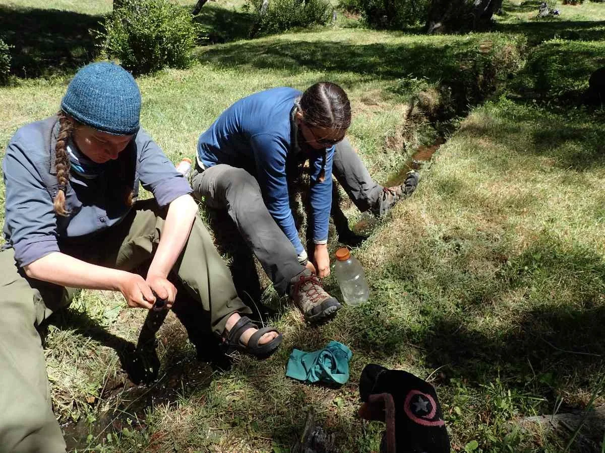 Hikers kneeling by a stream to wash their socks.