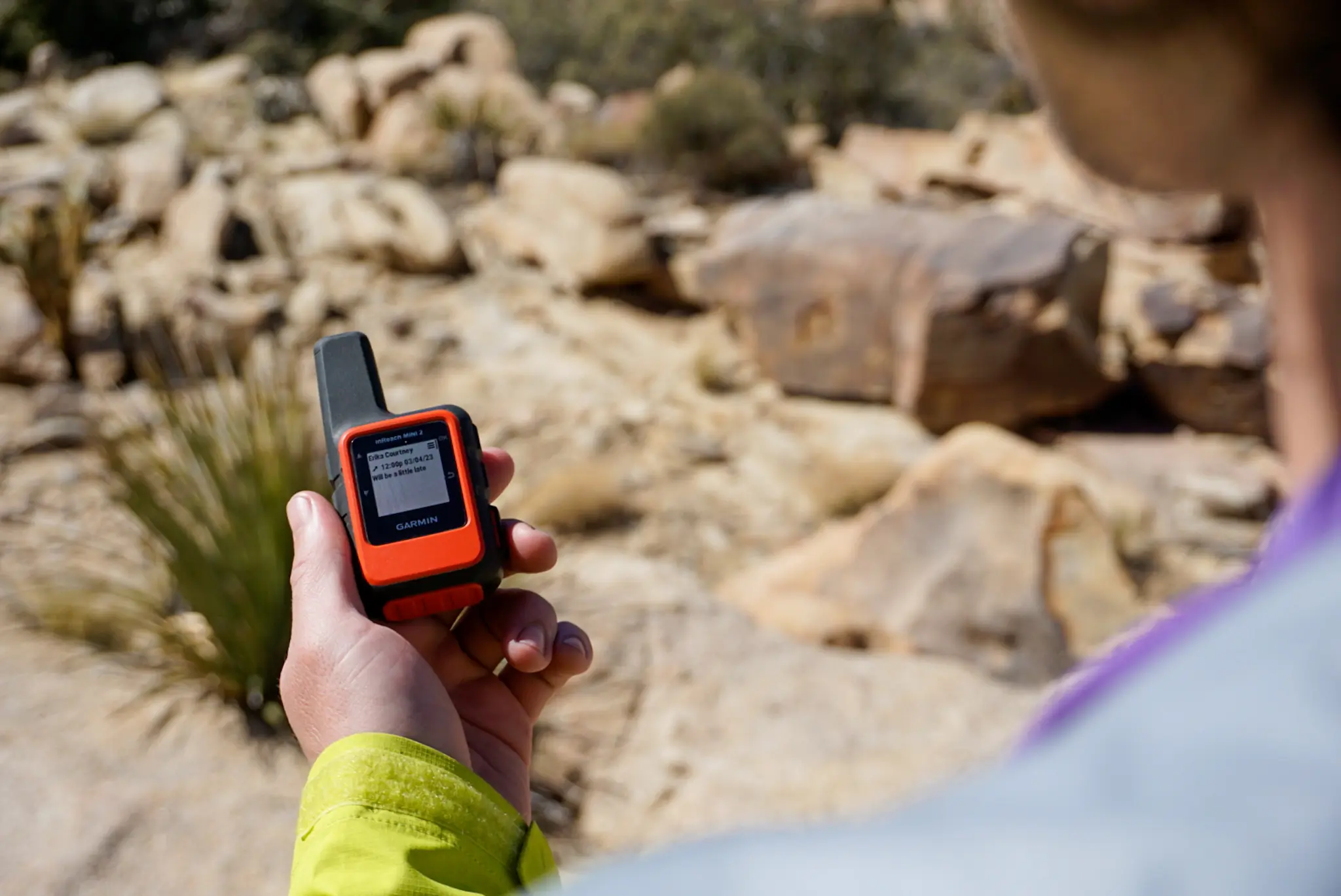 A Garmin inReach Mini clipped to a backpack strap in a scenic desert landscape.