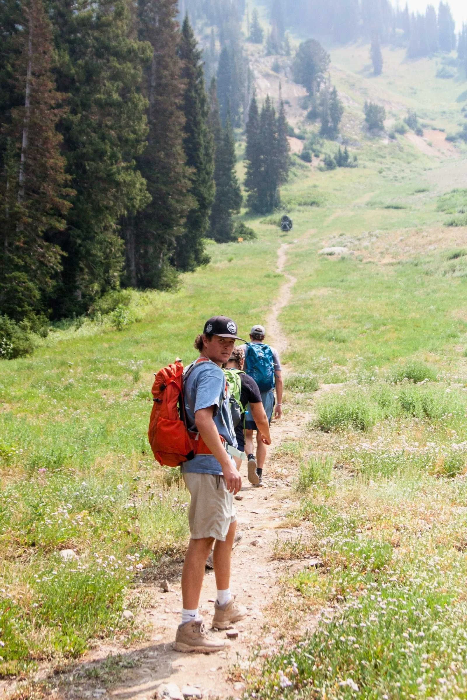 A hiker on a sunlit trail wearing a blue Osprey Stratos daypack.