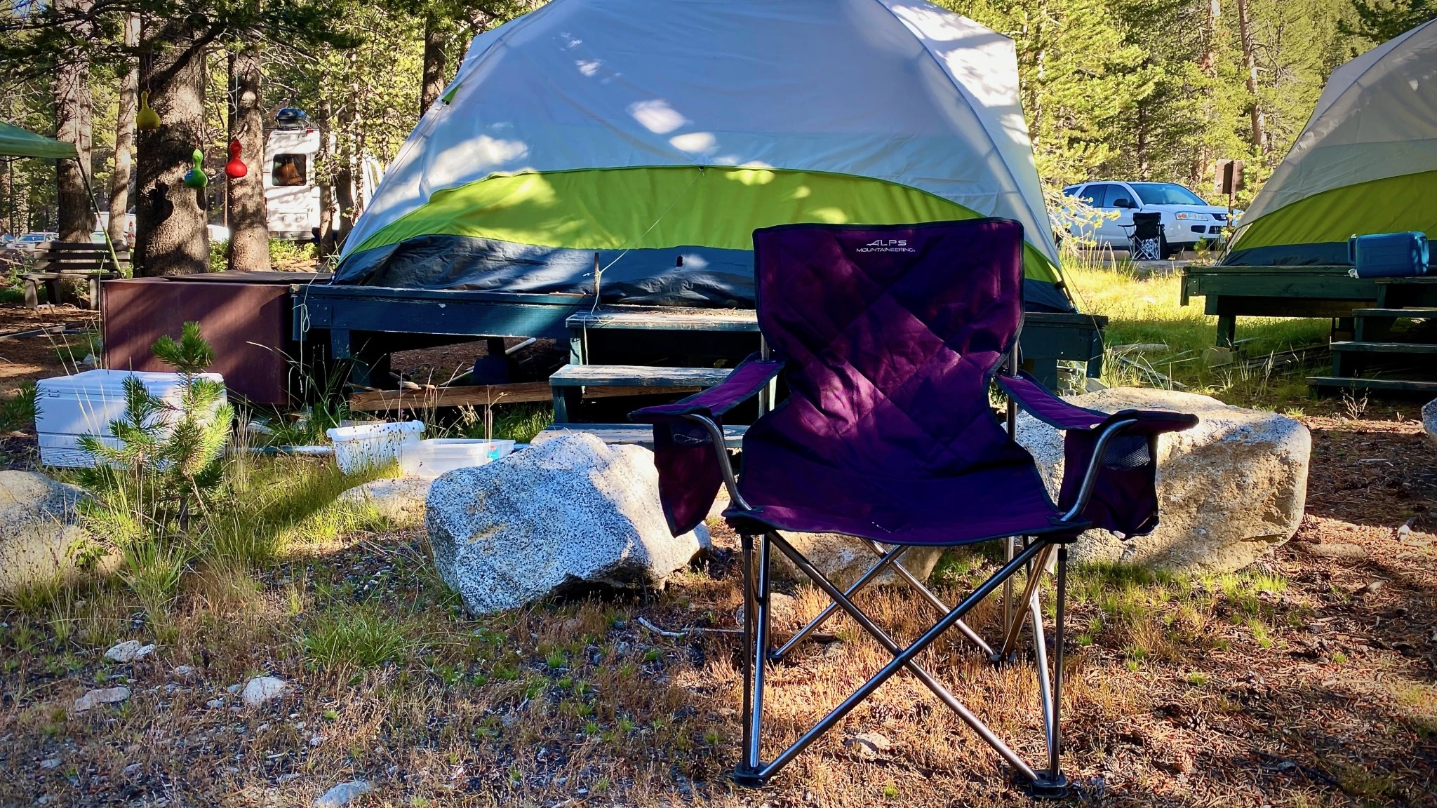 A person sitting in a large, sturdy green traditional camping chair at a campsite.