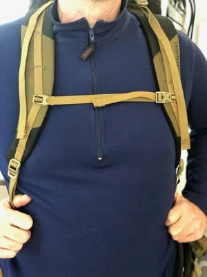 A person's hand adjusting the plastic buckle of a sternum strap on a hiking pack.