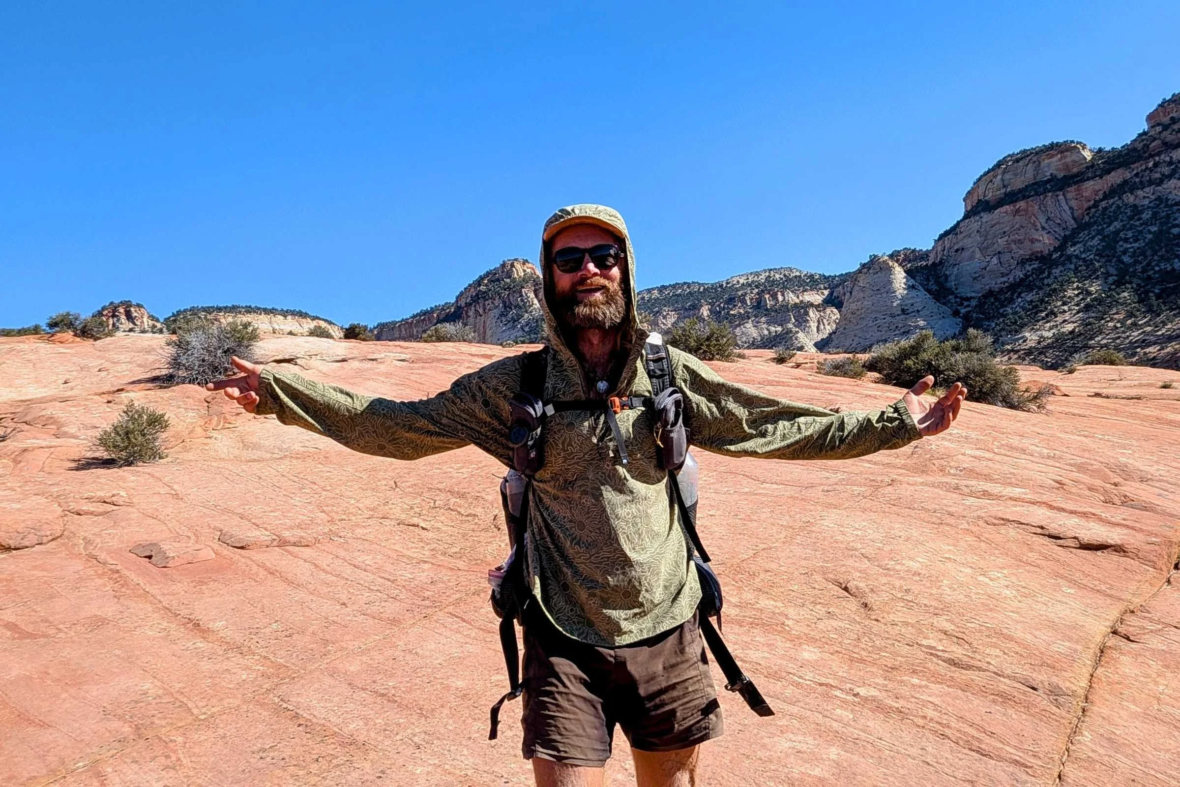 A trekking-pole supported ultralight shelter pitched on a flat slickrock bench at sunset.