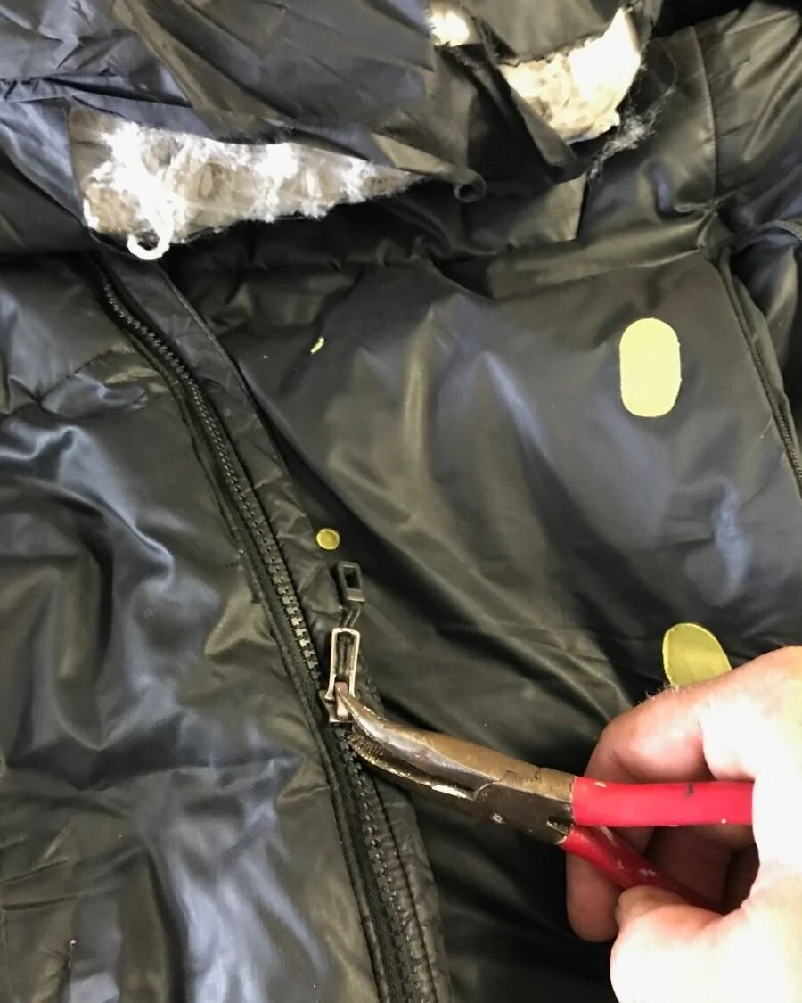 A person using pliers to remove a broken zipper slider from the top of the zipper track.
