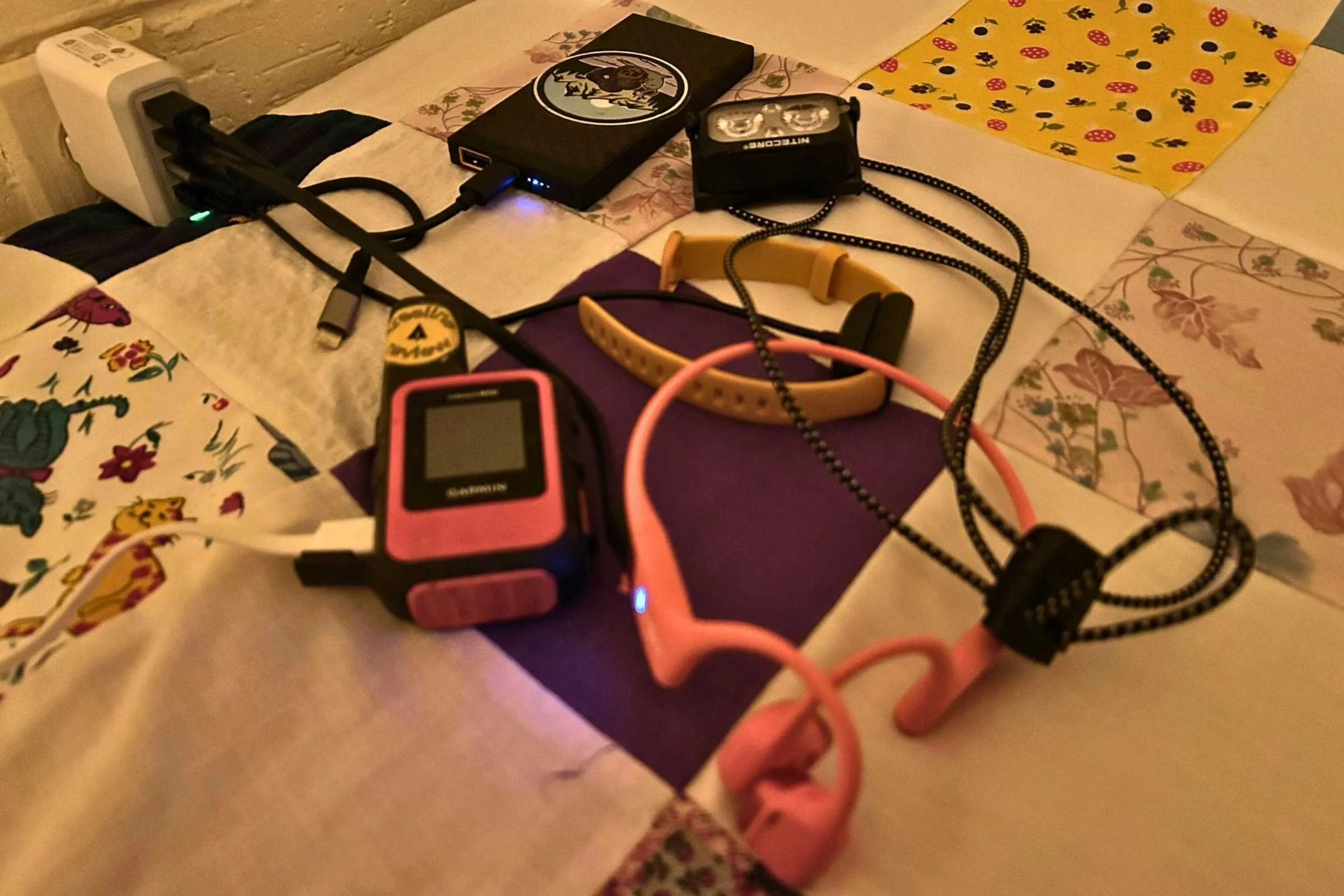 A 4-port USB wall charger plugged in and charging a headlamp, power bank, and satellite communicator.