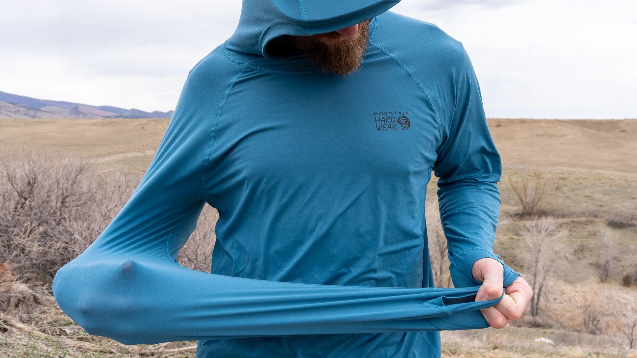 A man wearing a blue Mountain Hardwear Crater Lake hoody in a sunny landscape.